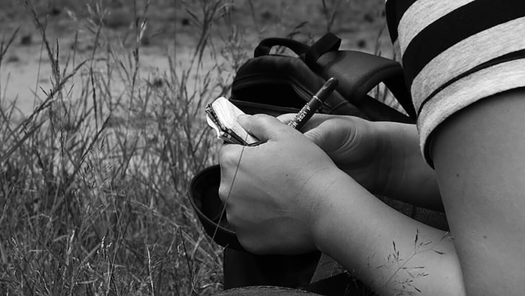 Pessoa escrevendo em um bloco de notas no campo
