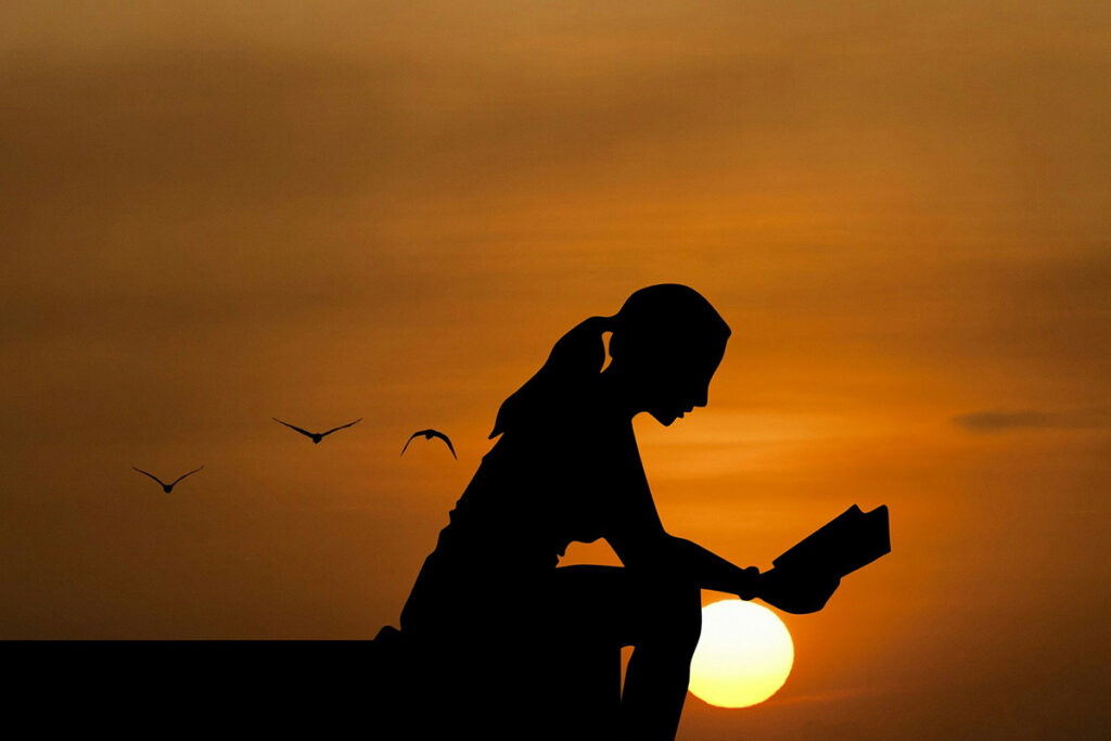 Silhueta de mulher lendo sob o pôr do sol