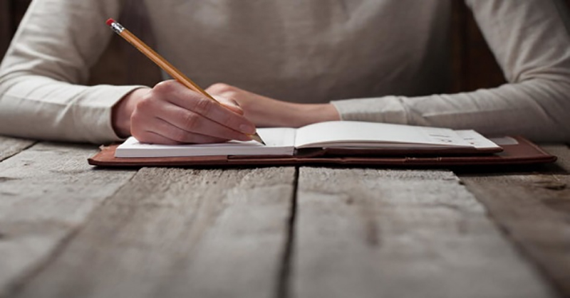 Homem escrevendo ficção em um caderno na mesa