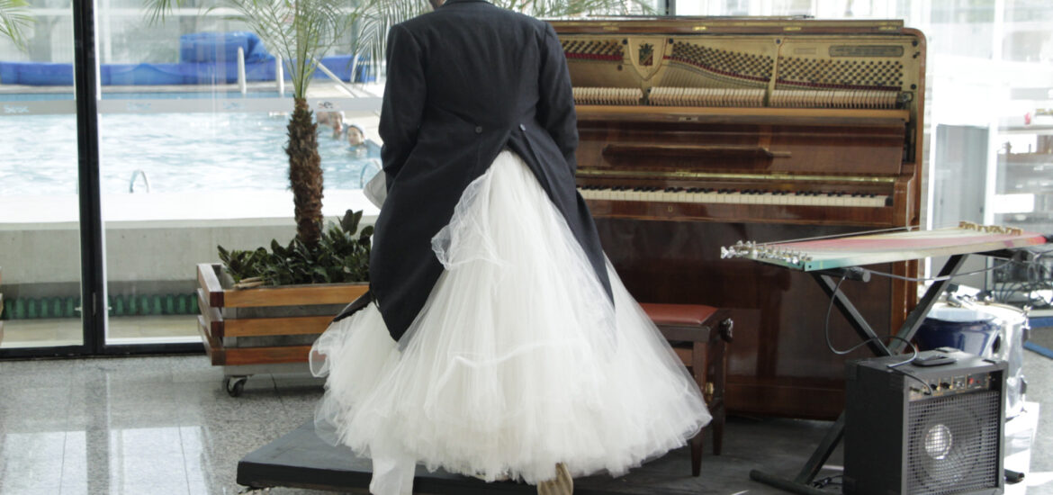 Foto homem de vestido de noiva e terno em tablado com piano e teclado