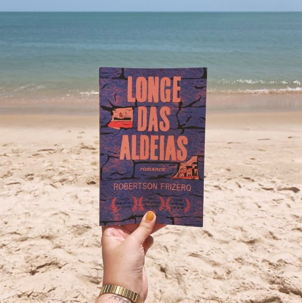 Mão feminina segurando livro Longe das Aldeias na praia