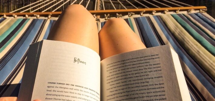 Pessoa lendo um livro sob o sol e deitada na rede