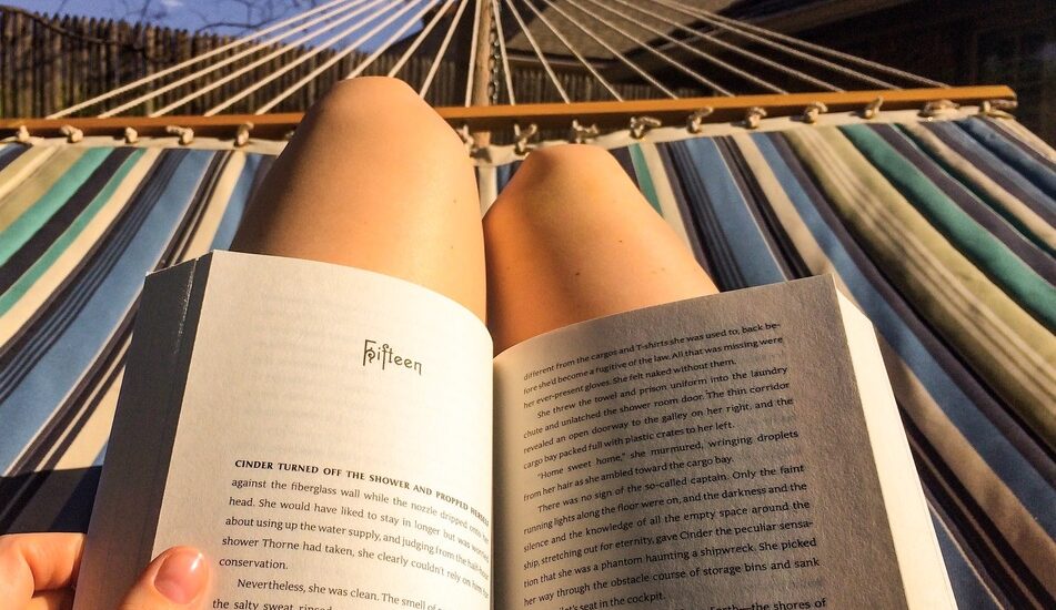Pessoa lendo um livro sob o sol e deitada na rede